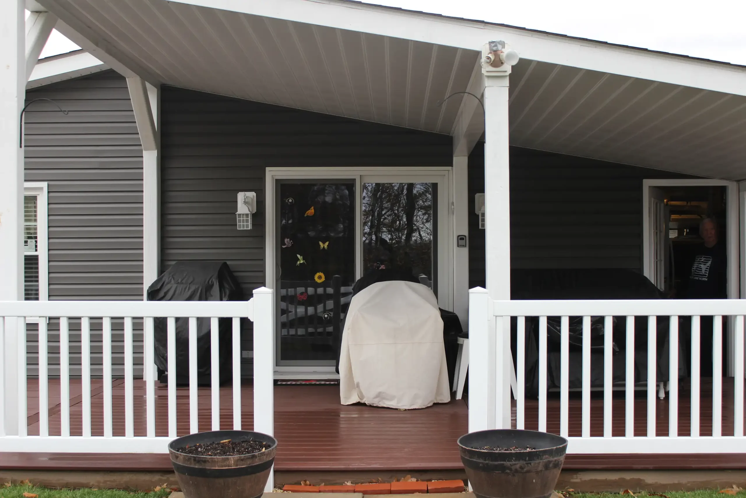 Photo of the entrance to a house, showing a deck with a roof and a white railing