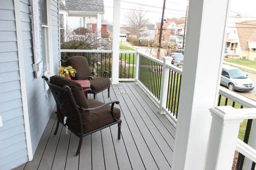 Photo of a simple deck located at the entrance to the house; it features two chairs and a table, as well as a white railing