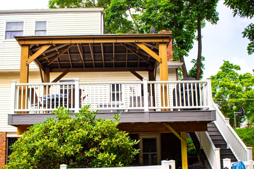 A photo showing the entire deck, which features a small roof to cover the furniture; there is also a staircase on the side that leads up to the deck